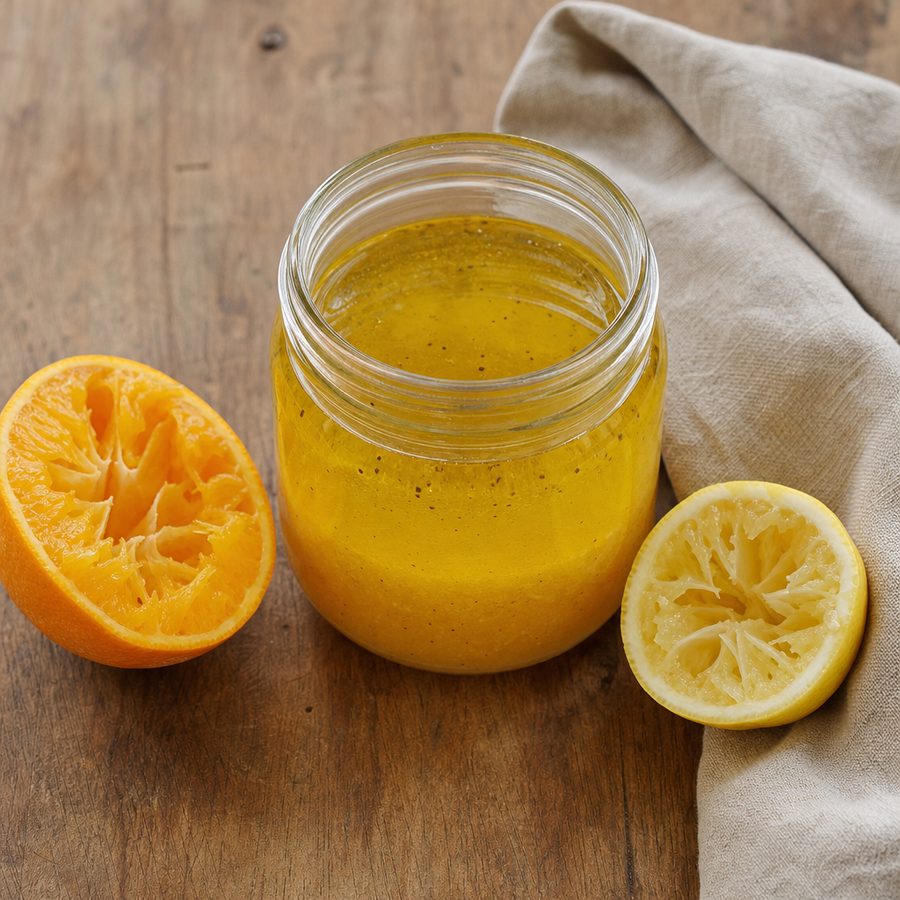 Small jar of citrus dressing with a cut orange and lemon